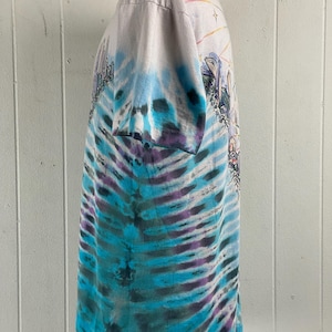 Puede incluir: Una camiseta blanca tie-dye con un patr&oacute;n de remolino azul, morado y verde. La camiseta presenta una impresi&oacute;n gr&aacute;fica de una ciudad con un arco&iacute;ris y estrellas.