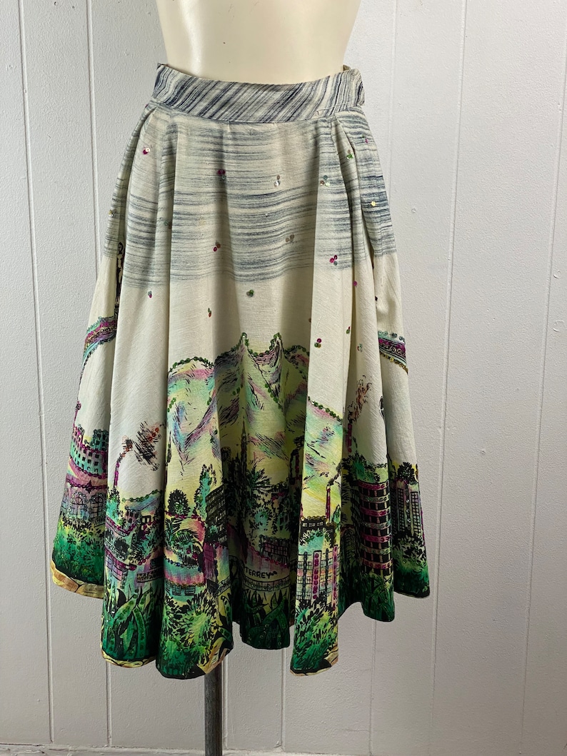 May include: A white full skirt with a colorful city scene print. The skirt has a black waistband and is decorated with sequins.