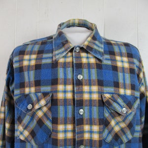 以下が含まれることがあります： 長袖で胸ポケットが2つ付いた、青、黄、黒の格子柄のフランネルシャツです。