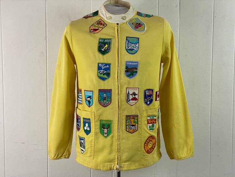 May include: A yellow jacket with a zipper closure and numerous embroidered patches featuring state and city names and logos. The patches are in various colors and designs.