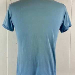 K&ouml;nnte beinhalten: Ein hellblaues T-Shirt mit Rundhalsausschnitt und kurzen &Auml;rmeln.