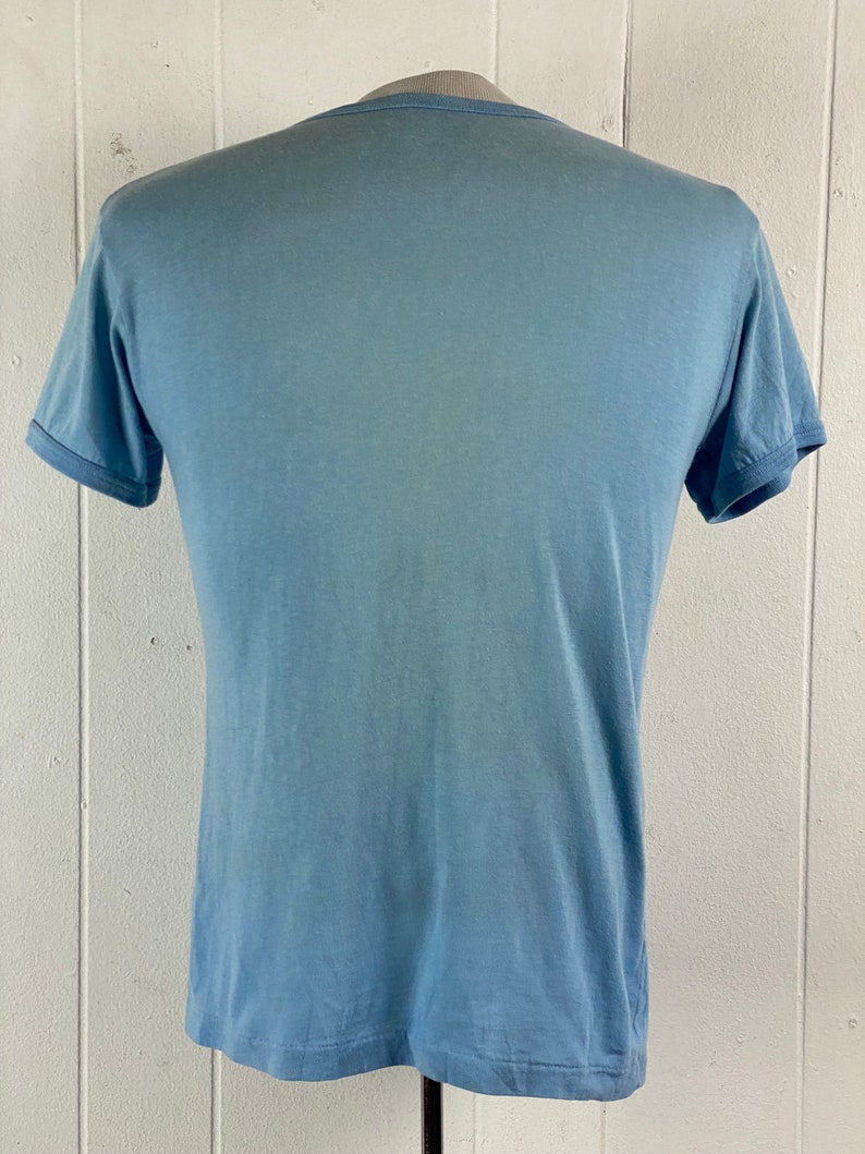 K&ouml;nnte beinhalten: Ein hellblaues T-Shirt mit Rundhalsausschnitt und kurzen &Auml;rmeln.