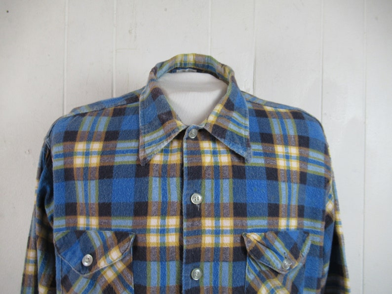 以下が含まれることがあります： ボタンダウンカラーと長袖の青、黄、茶色の格子柄のフランネルシャツ