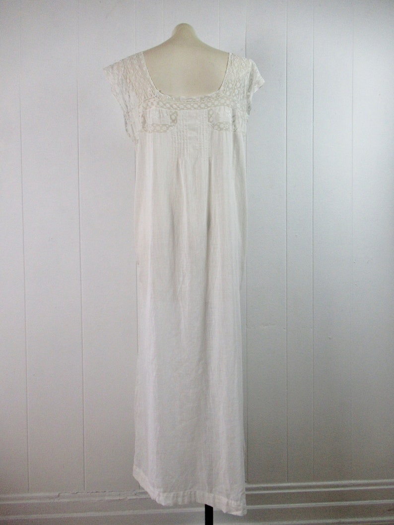 Puede incluir: Un camis&oacute;n blanco de algod&oacute;n con ribete de encaje alrededor del escote y las mangas. El camis&oacute;n tiene un dise&ntilde;o simple y cl&aacute;sico y es de largo hasta el suelo.