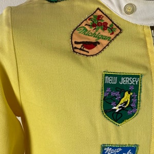 May include: Yellow jacket with embroidered patches of different states including Michigan, New Jersey, and New York.
