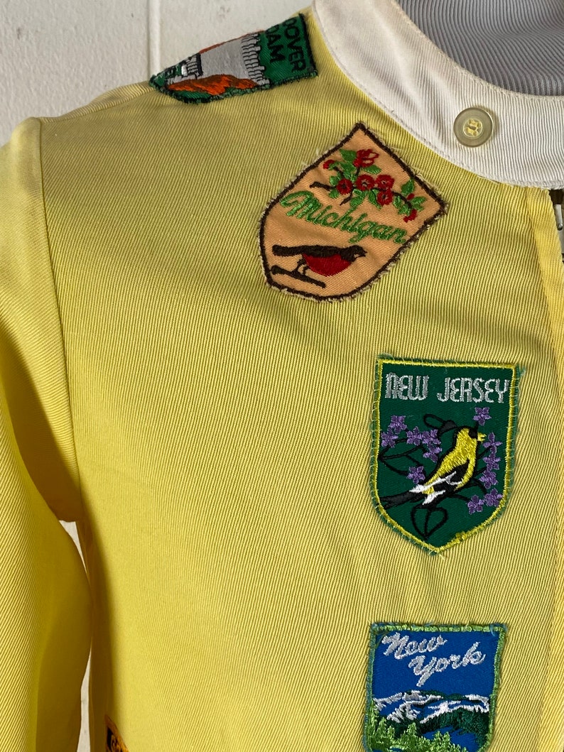 May include: Yellow jacket with embroidered patches of different states including Michigan, New Jersey, and New York.