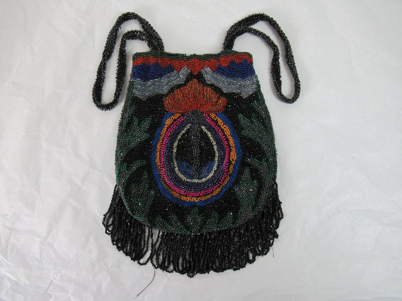 Puede incluir: Un bolso de noche de cuentas negras con un dise&ntilde;o floral colorido y flecos. El bolso tiene una larga correa de cuentas.