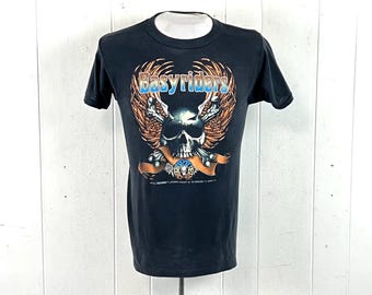 May include: A black short-sleeve t-shirt featuring a graphic print of a skull with wings and crossed bones. The text "Easyriders" appears in blue and white lettering above the skull, with an orange banner draped across the bottom of the design.