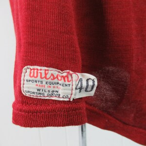 May include: A red Wilson sports equipment jersey with a white tag that reads "Wilson Sports Equipment Made in U.S.A. Wilson Sporting Goods Co." and a white tag with the number "40" on it.