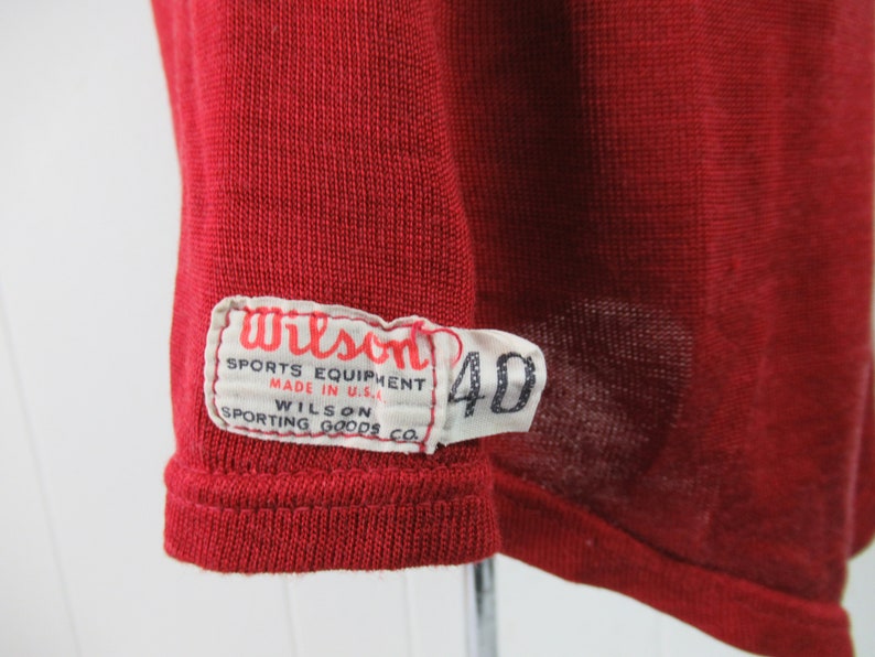 May include: A red Wilson sports equipment jersey with a white tag that reads "Wilson Sports Equipment Made in U.S.A. Wilson Sporting Goods Co." and a white tag with the number "40" on it.