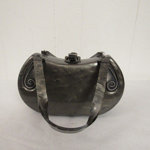 May include: A silver-colored, oval-shaped clutch purse with a decorative clasp and a black strap.