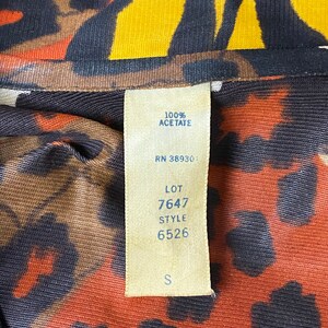 Puede incluir: Una tela de estampado de leopardo marr&oacute;n, naranja y amarillo con una etiqueta blanca adjunta. La etiqueta tiene el texto "100% Acetato", "RN 38930", "LOT 7647", "STYLE 6526" y "S".