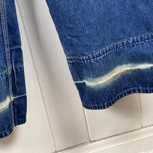 K&ouml;nnte beinhalten: Nahaufnahme einer Jeans aus hellblauem Denim mit einem wei&szlig;en, verblichenen Streifendetail am Saum. Die Jeans hat einen klassischen, l&auml;ssigen Stil mit sichtbaren N&auml;hten und einem leicht verwaschenen Look.