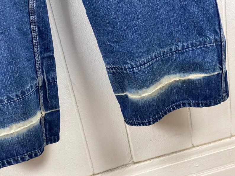 K&ouml;nnte beinhalten: Nahaufnahme einer Jeans aus hellblauem Denim mit einem wei&szlig;en, verblichenen Streifendetail am Saum. Die Jeans hat einen klassischen, l&auml;ssigen Stil mit sichtbaren N&auml;hten und einem leicht verwaschenen Look.