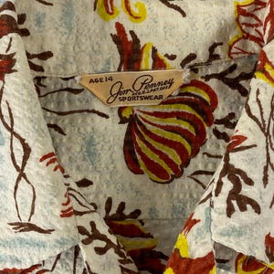 May include: A vintage beige button-up shirt with a colorful floral print. The shirt has a label that reads "Jim Penny Sportswear" and "Age 14".