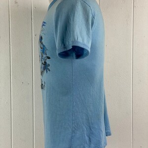 K&ouml;nnte beinhalten: Ein hellblaues T-Shirt mit kurzen &Auml;rmeln und einem grafischen Druck in Blau und Wei&szlig;.
