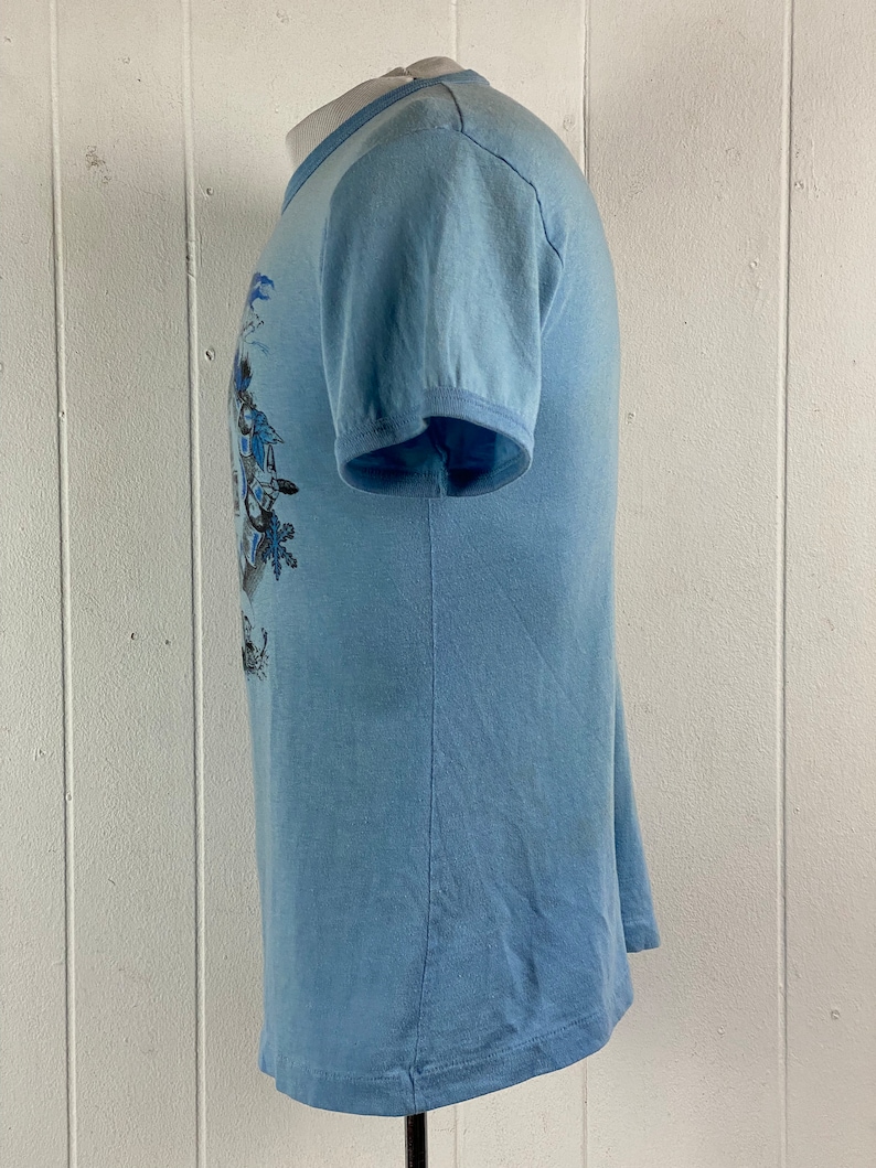 K&ouml;nnte beinhalten: Ein hellblaues T-Shirt mit kurzen &Auml;rmeln und einem grafischen Druck in Blau und Wei&szlig;.