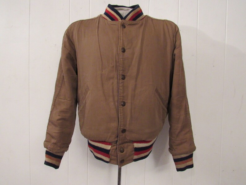 May include: A brown bomber jacket with a white, red, and blue striped collar and cuffs.