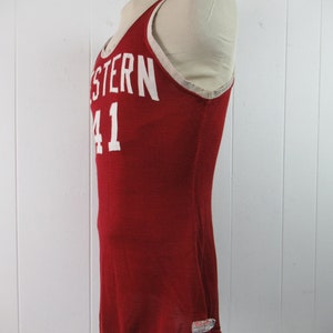May include: Red basketball jersey with white lettering that says "WESTERN 41". The jersey has a white trim around the neck and armholes. The jersey is made by Wilson.