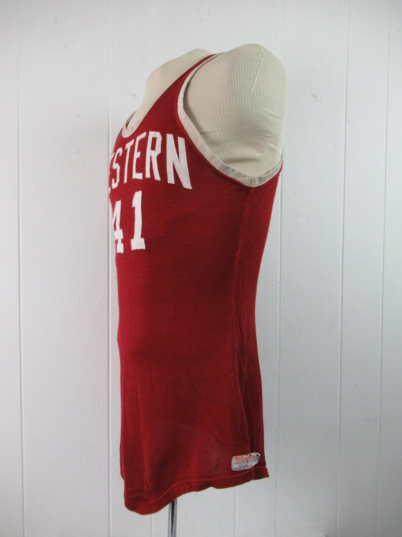 May include: Red basketball jersey with white lettering that says "WESTERN 41". The jersey has a white trim around the neck and armholes. The jersey is made by Wilson.