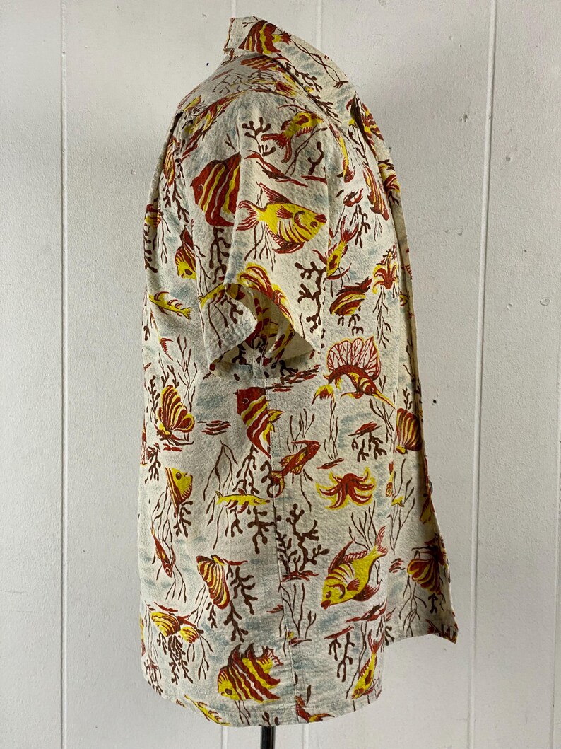May include: A short-sleeved button-up shirt with a white background and a colorful print of fish and coral. The shirt has a relaxed fit and a classic collar.