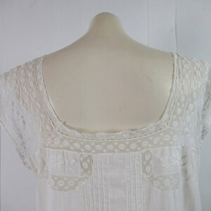 Puede incluir: Camis&oacute;n blanco de algod&oacute;n con delicado encaje alrededor del cuello y las mangas. El encaje presenta un patr&oacute;n floral.