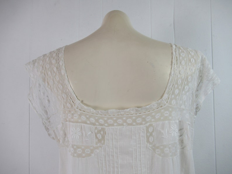 Puede incluir: Camis&oacute;n blanco de algod&oacute;n con delicado encaje alrededor del cuello y las mangas. El encaje presenta un patr&oacute;n floral.
