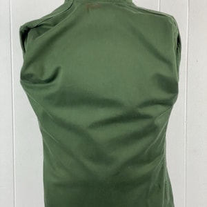 May include: A solid olive green jacket with a high collar. The back of the jacket is visible, showing the tailored fit and seams. The fabric appears to be a durable, possibly military-style material.