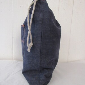 K&ouml;nnte beinhalten: Eine dunkelblaue Kordeltasche aus Denim mit einer kleinen Tasche an der Seite. Die Tasche ist aus einem dicken, strapazierf&auml;higen Stoff gefertigt und hat einen wei&szlig;en Kordelzug.