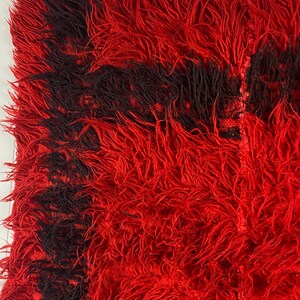 May include: Red and black shaggy rug with a fringe border. The rug has a unique texture and is made of soft, fluffy fibers.