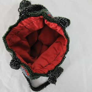 Puede incluir: Un bolso de cuentas negras y verdes con forro de sat&eacute;n rojo. El bolso tiene un asa de cuentas y un dise&ntilde;o decorativo.
