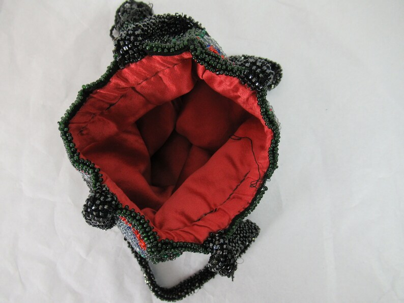 Puede incluir: Un bolso de cuentas negras y verdes con forro de sat&eacute;n rojo. El bolso tiene un asa de cuentas y un dise&ntilde;o decorativo.