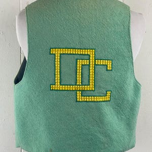 May include: A green sleeveless vest with a yellow embroidered "DC" logo on the back.