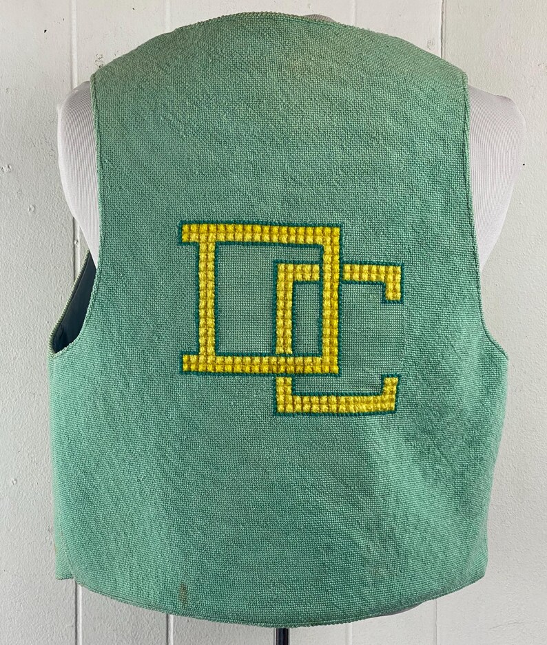 May include: A green sleeveless vest with a yellow embroidered "DC" logo on the back.