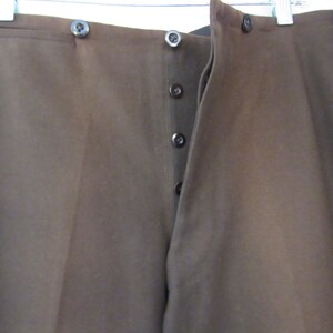 May include: A pair of brown pants with a button fly and black trim along the sides.