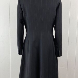 May include: A black pinstripe blazer with a long, fitted silhouette. The blazer has a pointed collar and long sleeves with button cuffs.