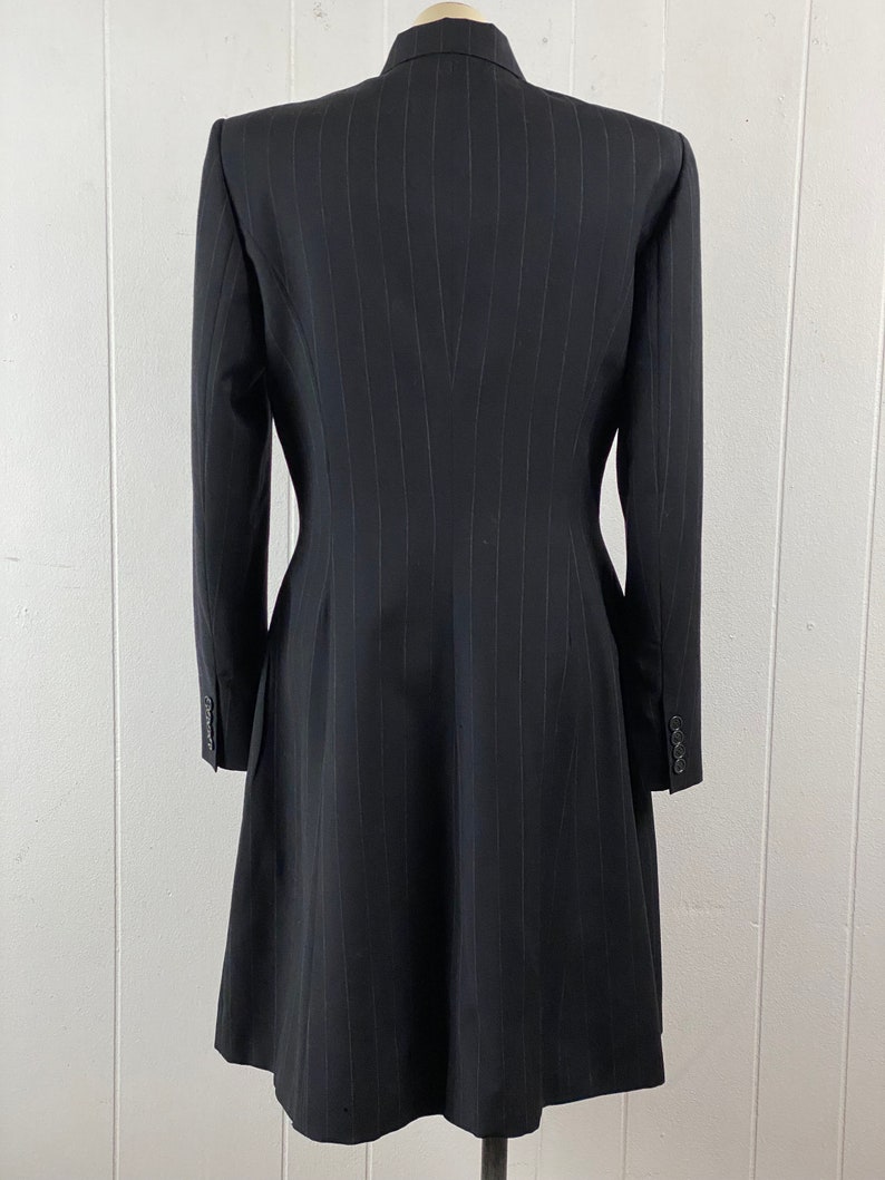 May include: A black pinstripe blazer with a long, fitted silhouette. The blazer has a pointed collar and long sleeves with button cuffs.