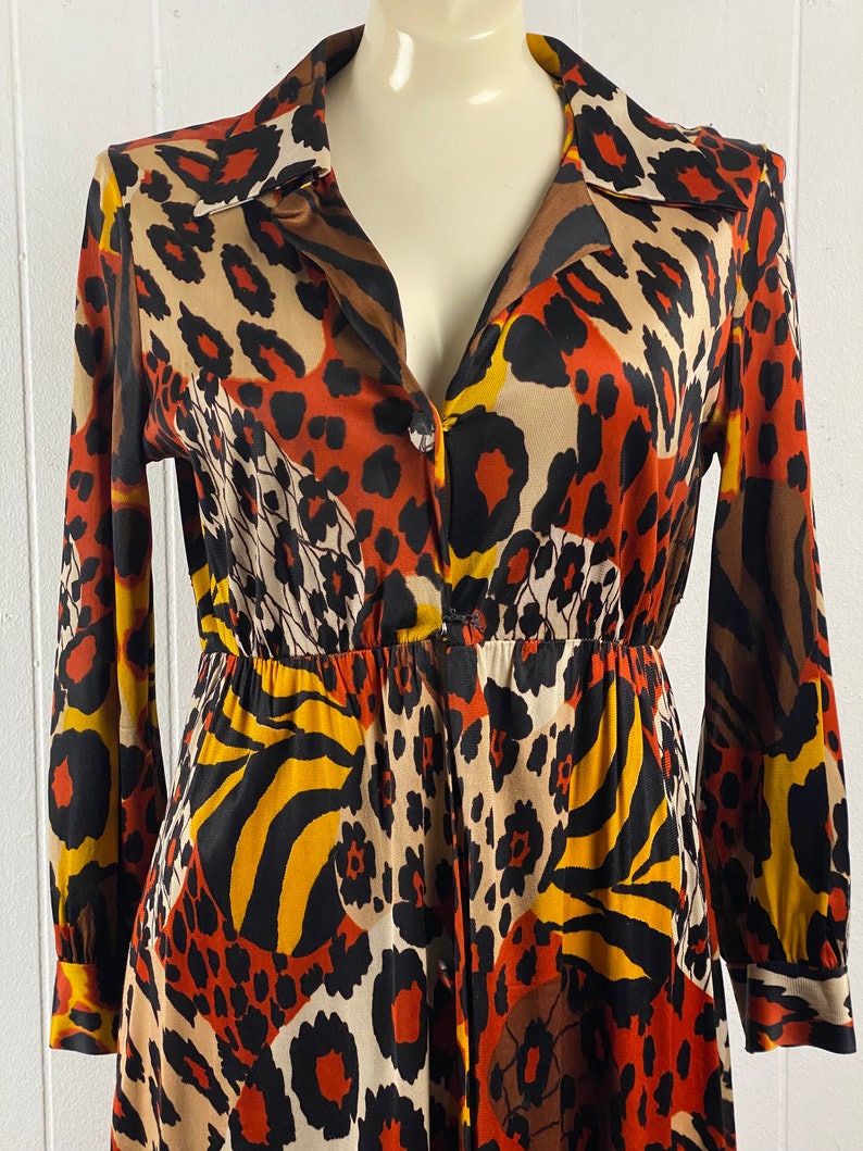 Puede incluir: Un vestido de manga larga con cierre de botones en la parte delantera y cuello en V. El vestido est&aacute; hecho de una tela sedosa y presenta un estampado de animales colorido en tonos marrones, naranjas, amarillos y negros.