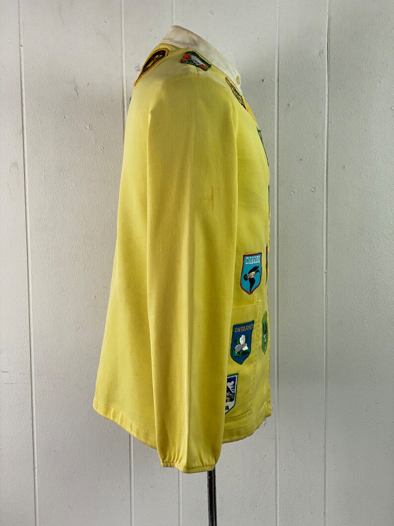 May include: A yellow jacket with a variety of colorful patches sewn on the front. The patches feature images of birds, flowers, and other nature-themed designs.