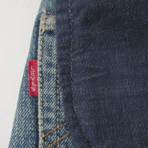 May include: Close-up of a pair of blue denim jeans with a red "Levi's" label sewn on the back pocket.