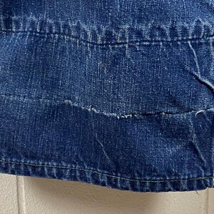 K&ouml;nnte beinhalten: Nahaufnahme eines Abschnitts einer blauen Jeans. Das Bild zeigt die Nahtdetails, einschlie&szlig;lich der N&auml;hte und der verst&auml;rkten Bereiche. Der Denim hat ein abgenutztes Aussehen mit sichtbaren Gebrauchsspuren und einem ausgefransten Rand.