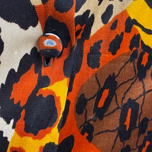 Puede incluir: Primer plano de una tela con un estampado de animales de colores. La tela tiene una combinaci&oacute;n de colores marr&oacute;n, naranja, negro y amarillo. Se puede ver un bot&oacute;n en el centro de la imagen.