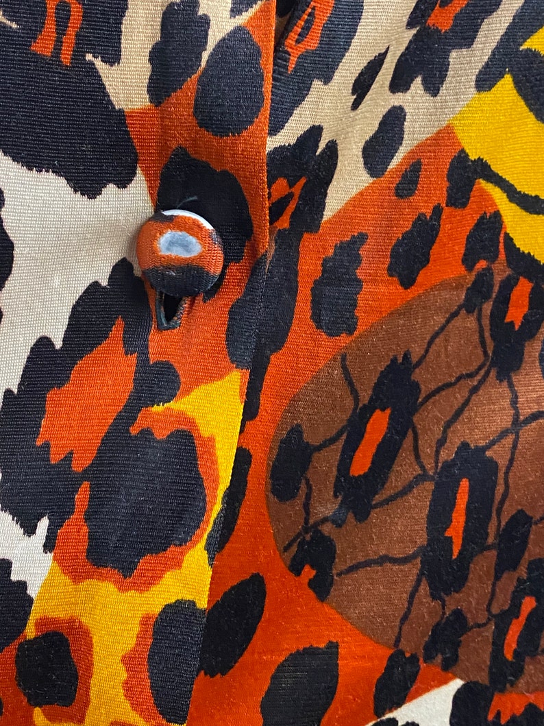 Puede incluir: Primer plano de una tela con un estampado de animales de colores. La tela tiene una combinaci&oacute;n de colores marr&oacute;n, naranja, negro y amarillo. Se puede ver un bot&oacute;n en el centro de la imagen.