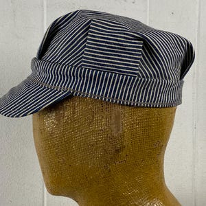May include: A blue and white striped cap with a short brim. The cap is made of fabric and has a classic design. The cap is displayed on a mannequin head.