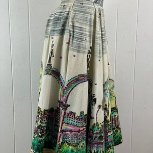 May include: A white full skirt with a colorful city scene print. The skirt has a high waist and a gathered design. The print features buildings, trees, and arches. The skirt is decorated with sequins.