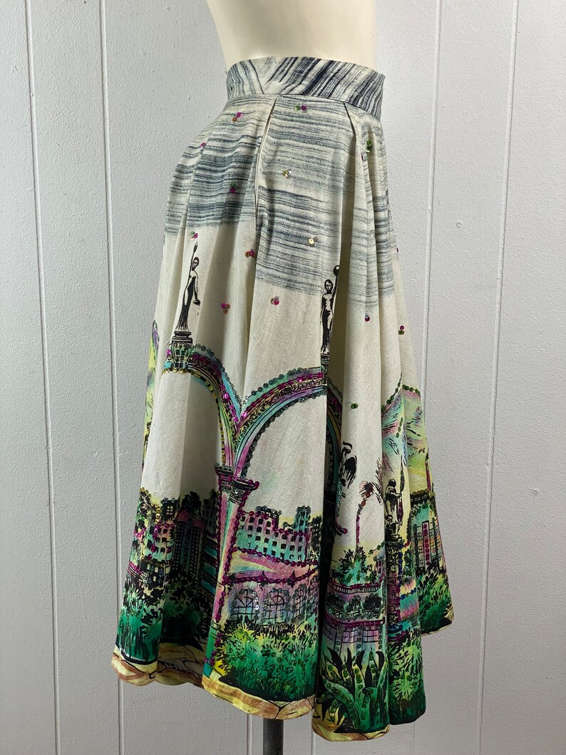 May include: A white full skirt with a colorful city scene print. The skirt has a high waist and a gathered design. The print features buildings, trees, and arches. The skirt is decorated with sequins.