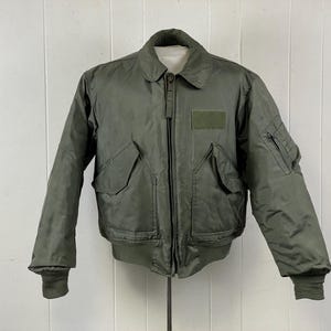 Puede incluir: Chaqueta bomber verde oliva con cuello, cremallera frontal y múltiples bolsillos. La chaqueta tiene puños acanalados y un parche en el pecho. Una chaqueta clásica de estilo militar.