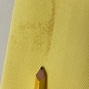 May include: Close-up of a yellow fabric with a diagonal weave pattern. A pencil with a brown eraser is resting on the fabric.
