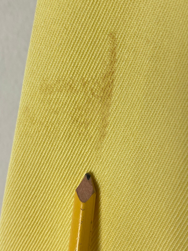 May include: Close-up of a yellow fabric with a diagonal weave pattern. A pencil with a brown eraser is resting on the fabric.
