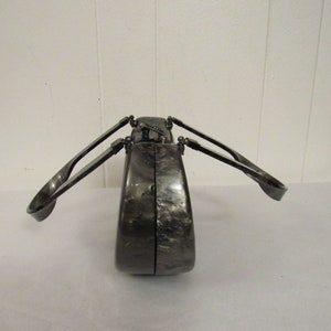 May include: A black and silver clutch purse with a unique design. The purse has two handles that fold out from the sides.